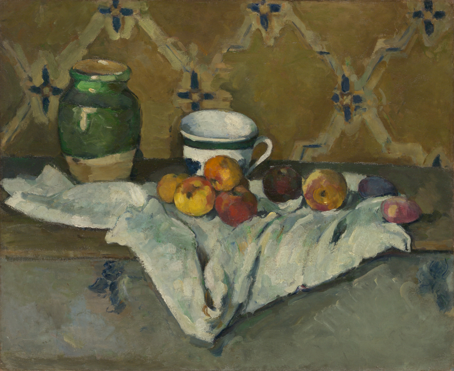 A green jar, patterned cup, and apples sit on a folded white cloth before patterned wallpaper.