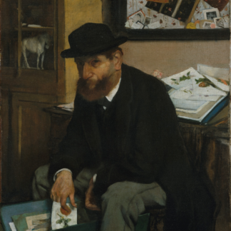 A bearded man in a black hat sits among portfolios, prints, and a cabinet of objects.