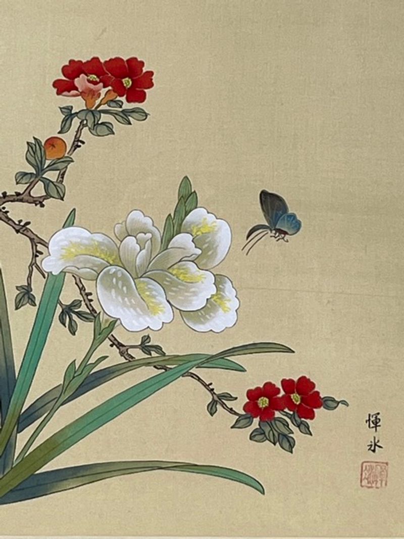 White and red flowers, long green leaves and a blue butterfly against the artwork's gold-colored silk ground